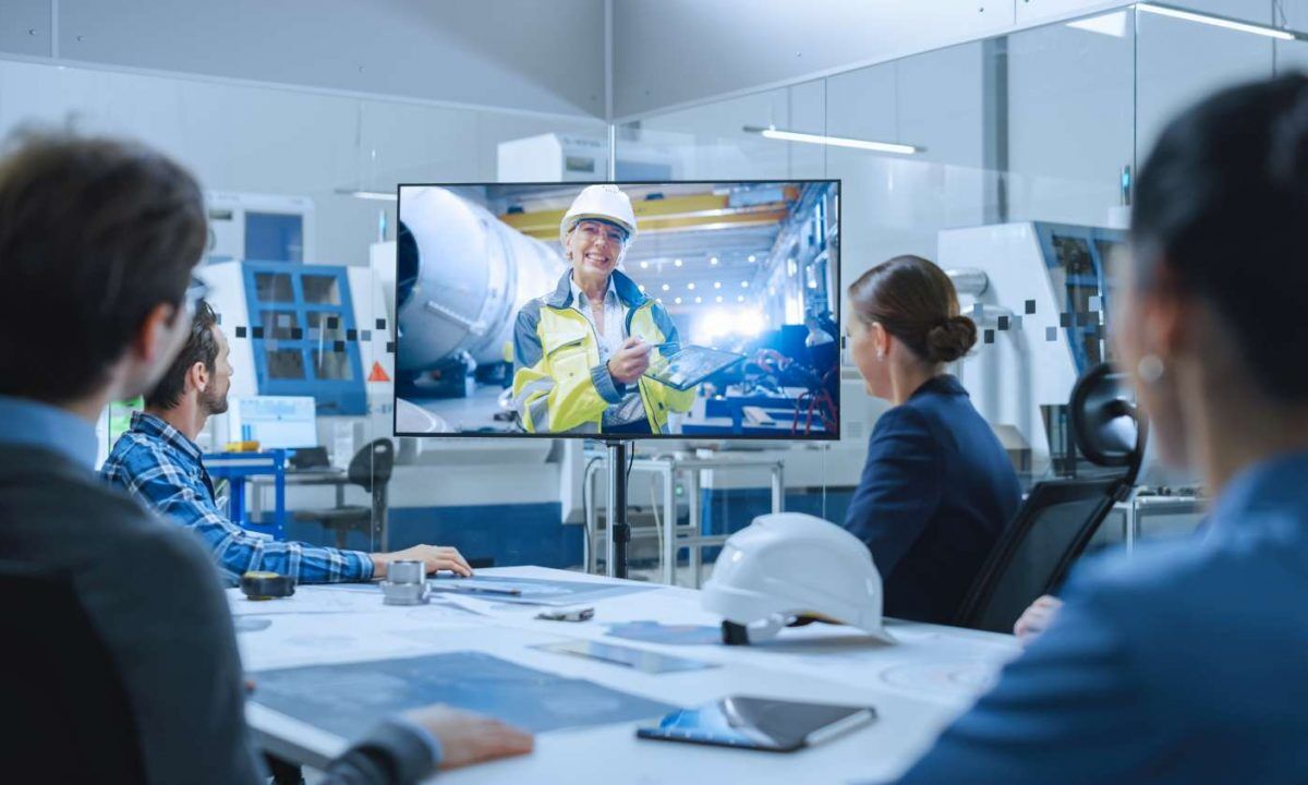 Diverse Group of Specialists, Managers in the Factory Office Meeting Room, Have Conference Video Call with Factory Chief Female Engineer, She Talks about Production Growth, Uses Tablet Computer