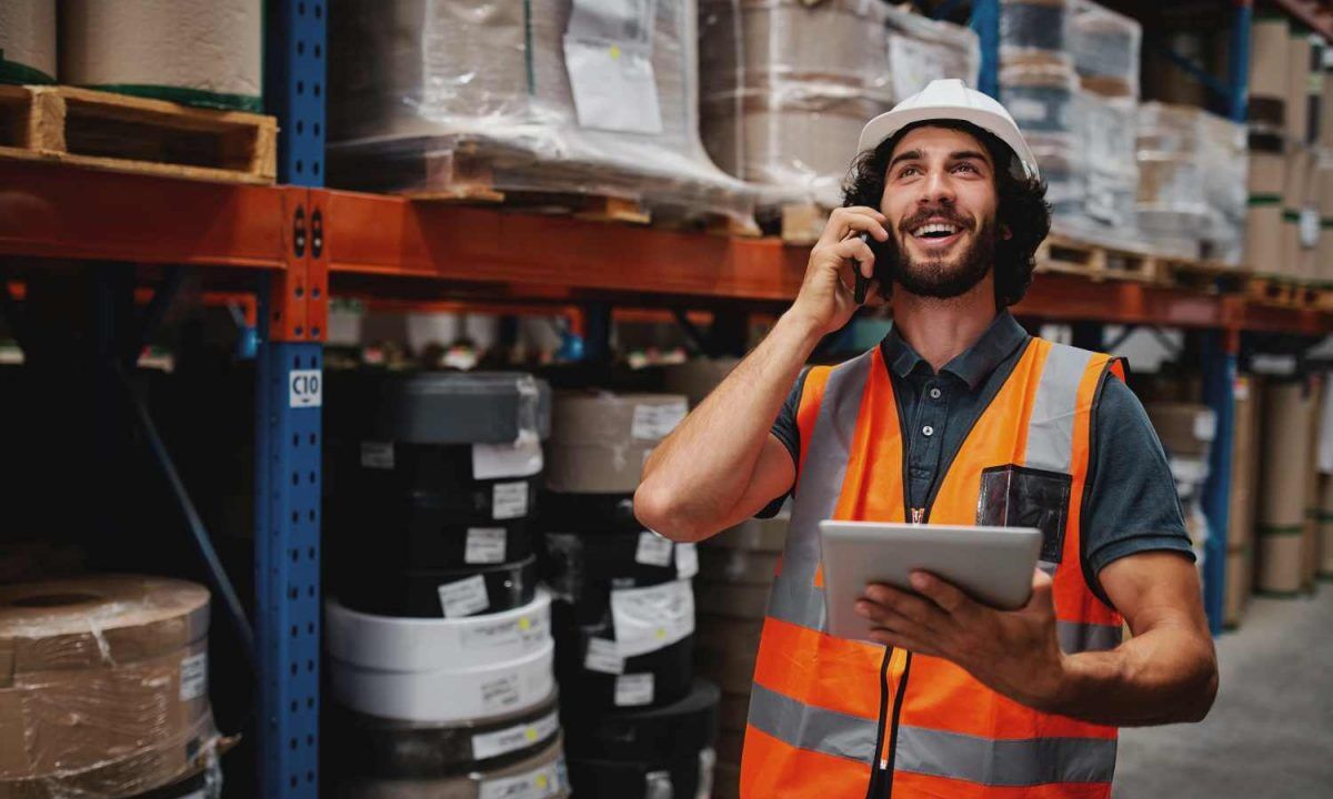 Young warehouse worker with beard talking over phone while working in storehouse