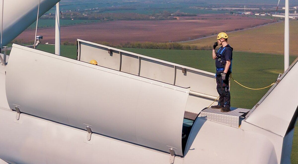 Aerial shot of a wind turbine Technician standing on the top of a wind turbine.