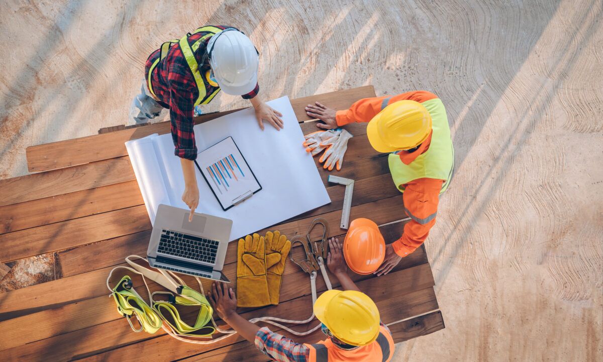 Workers in safety gear discussing digital toolbox talk materials on a construction site.