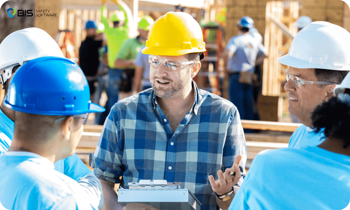 Construction site supervisor wearing a yellow hard hat and safety glasses discusses workplace safety procedures with a group of workers