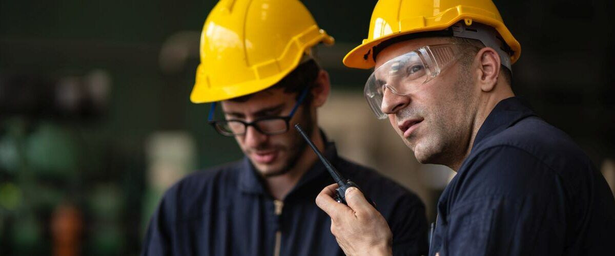 Panoramic banner of industrial workers talking through the walkie talkie to report incident in factory while looking away to outside, concept manufacturer procedure and incident reporter.