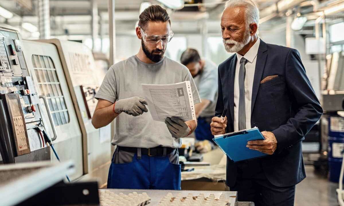 Worker and senior businessman cooperating while going through paperwork in factory plant.