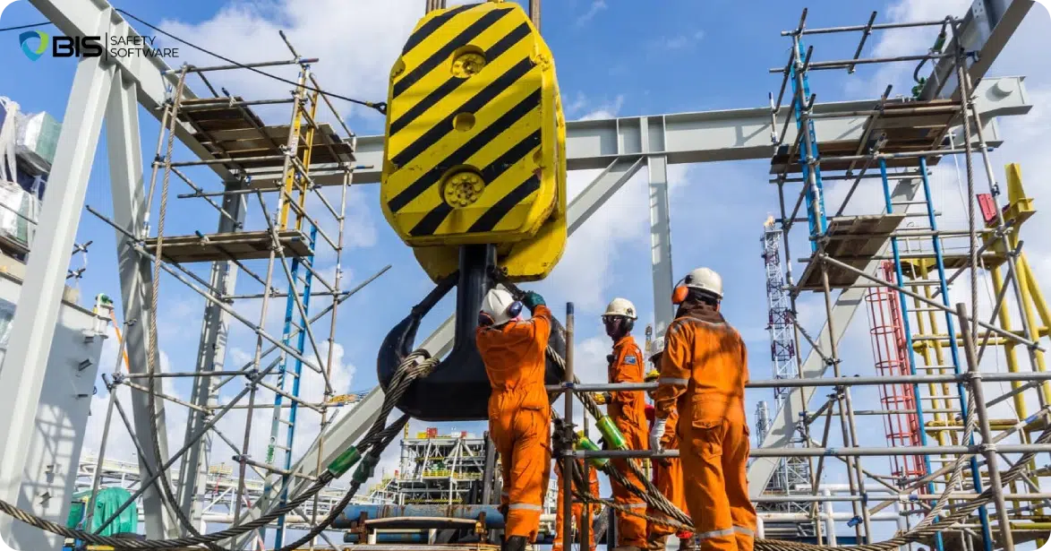 Construction workers wearing safety gear and helmets operating a large industrial crane hook.