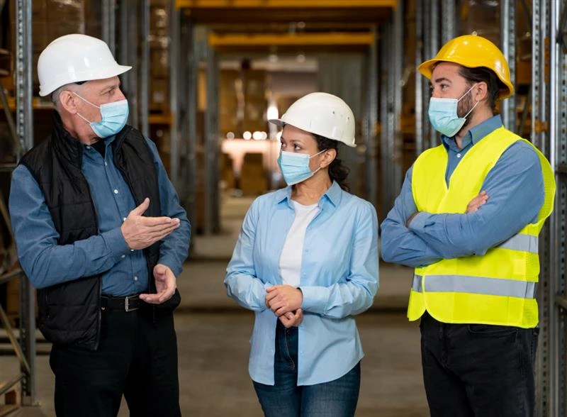 Warehouse workers in safety gear having a serious discussion, highlighting the importance of speaking up during safety meetings.