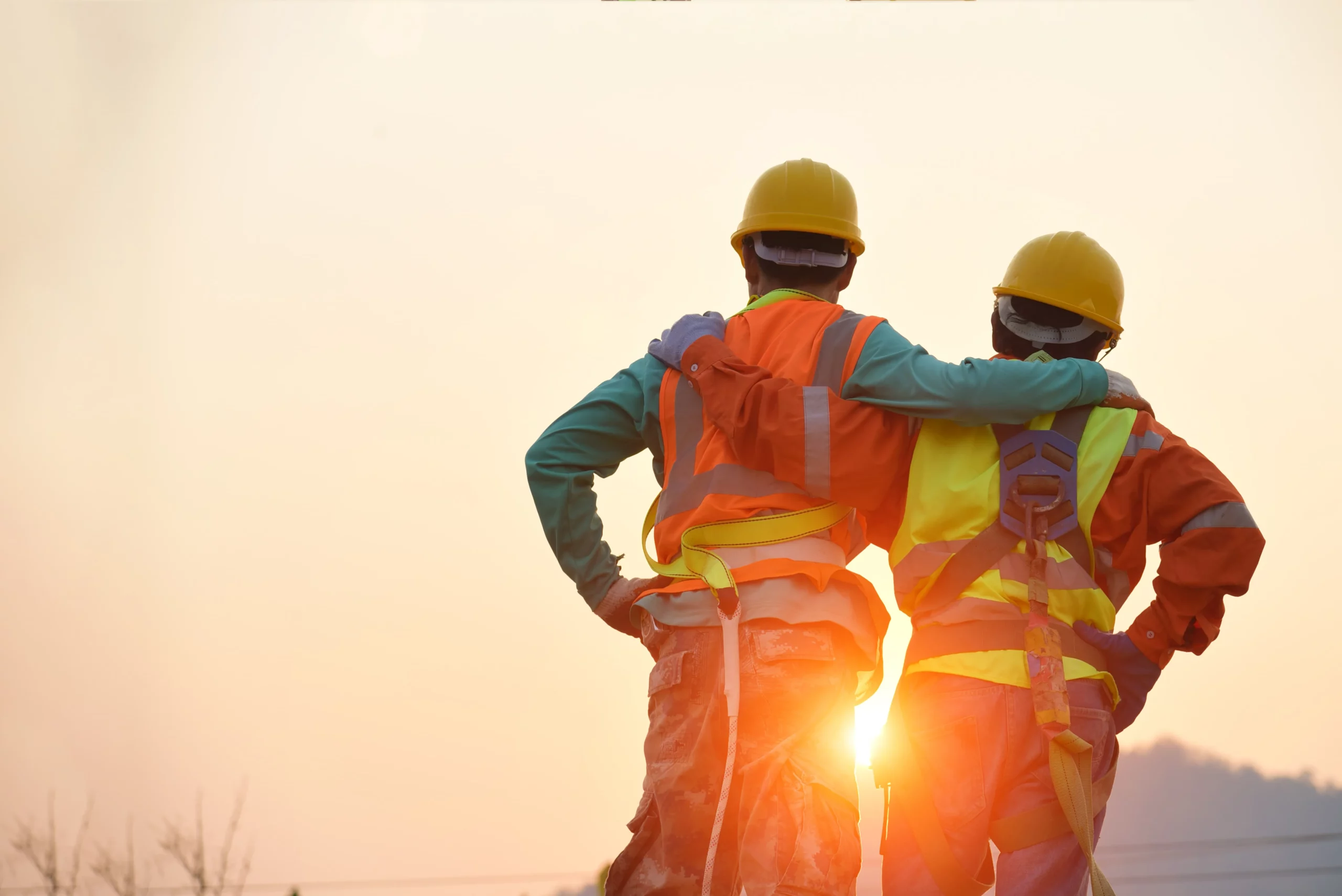 Two workers in safety gear at sunrise, showing teamwork and jobsite safety.