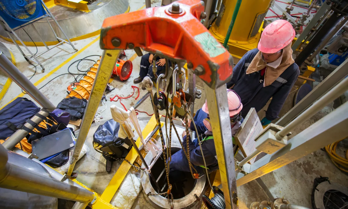 Confined space entry team using tripod and retrieval system for worker access.
