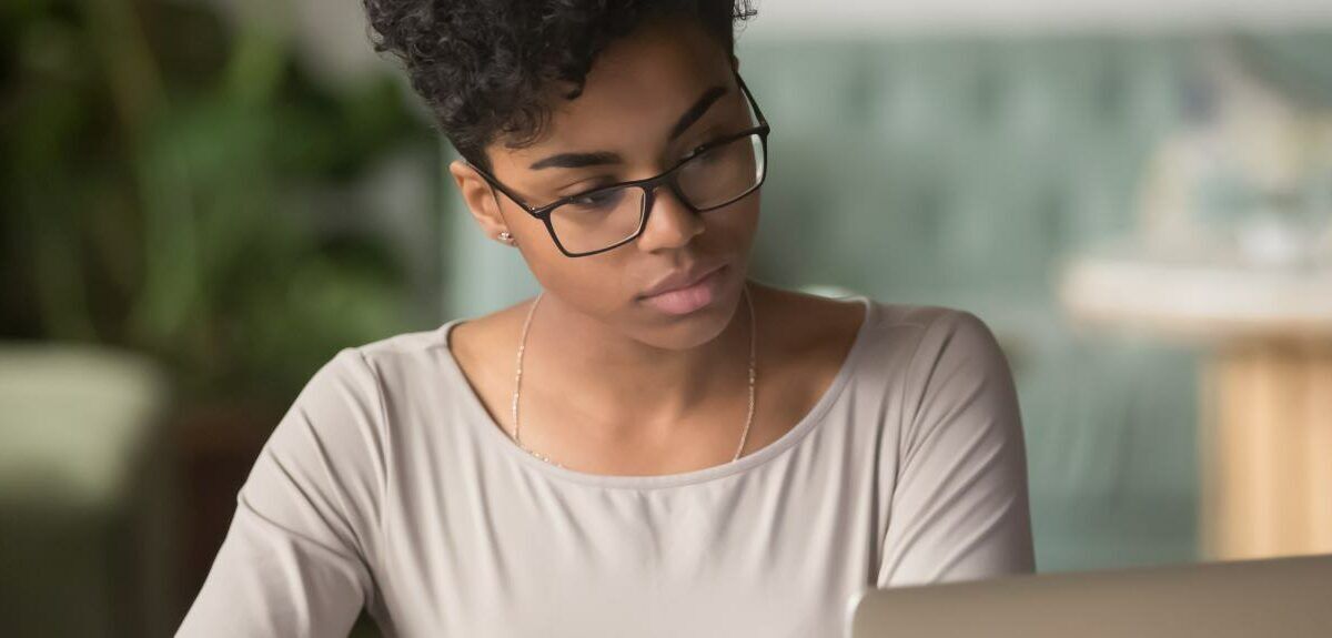 Horizontal photo banner for website header design, African student girl wear glasses sit indoors look at pc screen study on-line, do assignment, prepare for university admission exams, e-study concept