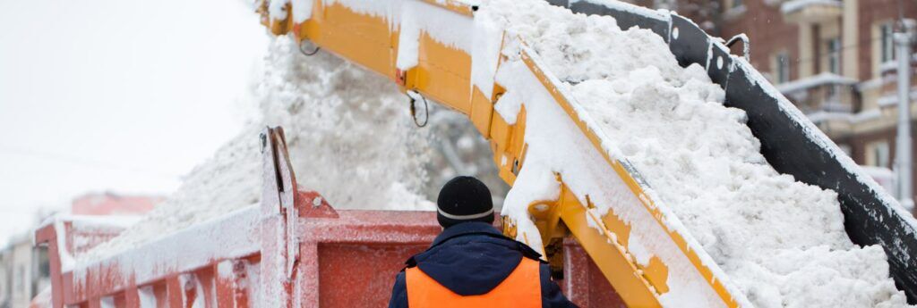 Claw loader vehicle removes snow from the road.  A snowplow pours snow into a truck.
