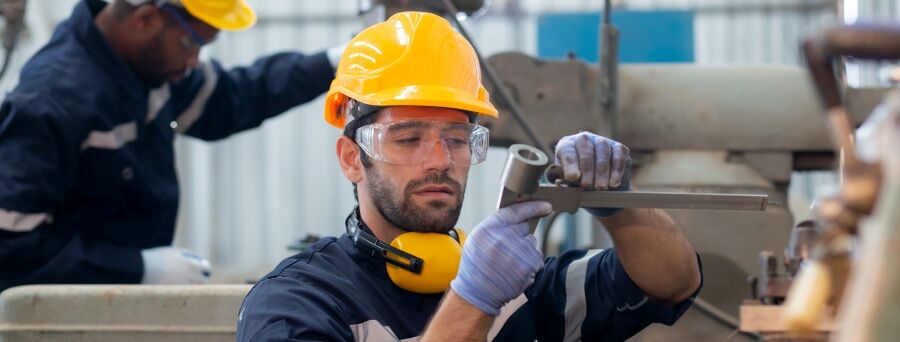 Young caucasian engineer man examining and measuring steel with expertise at lathe factory, worker or technician check and maintenance metal with professional, industry and machinery concept.