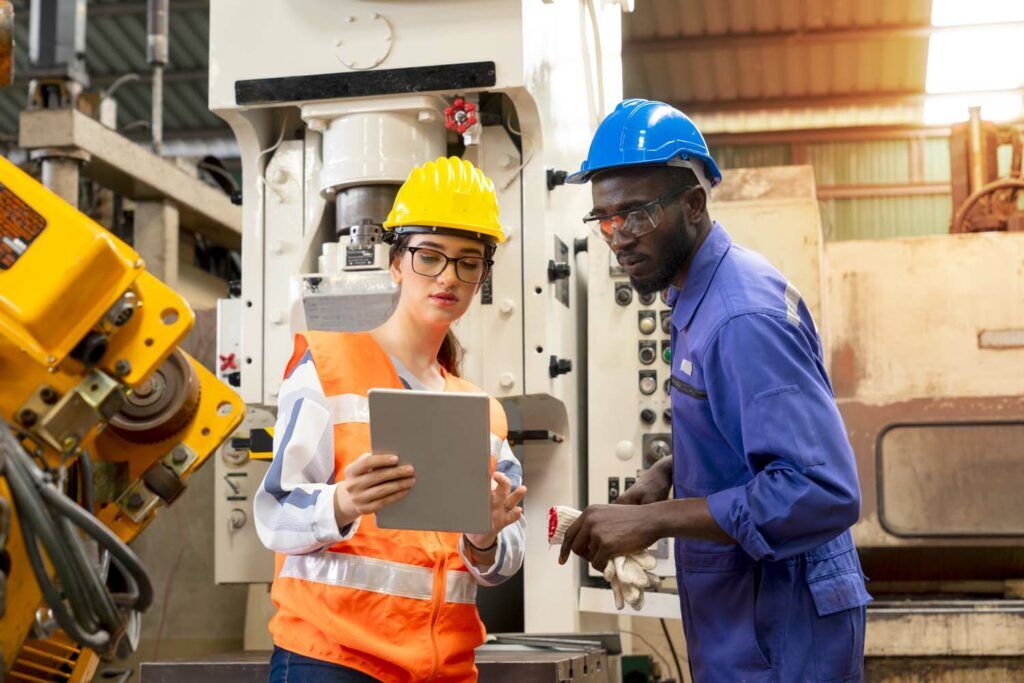 Supervisor, worker with hard hat working in manufacturing factory on business day. Female industrial engineers have to consult with colleagues while using tablet. Concept of workplace gender equality
