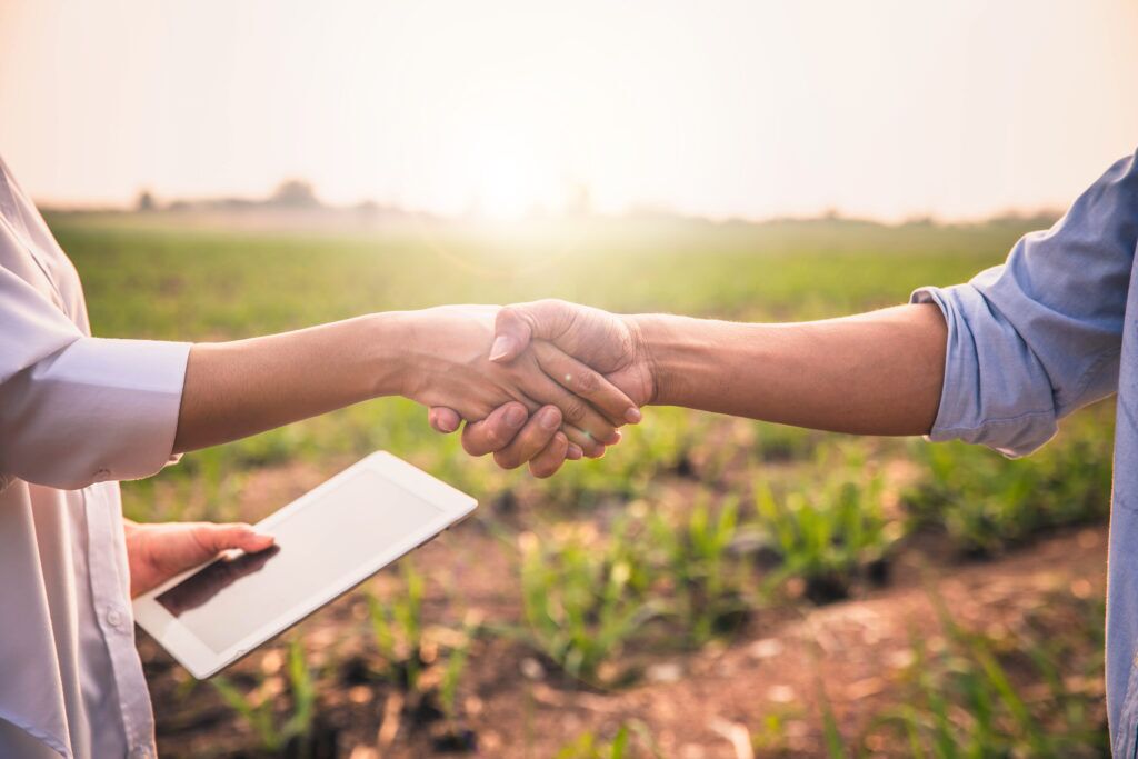 Handshake two farmer on the background of a wheat field at sunset. The concept of the agricultural business. farmer holding hands with beautiful woman with notebook in corn field. Elite Agri Solutions: A BIS Authorized Partner