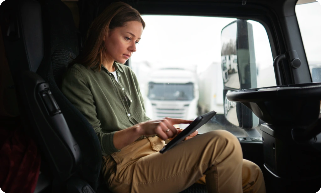 Side view of a woman truck driver in a cab, checking her log-book and finishing her pre trip inspection.