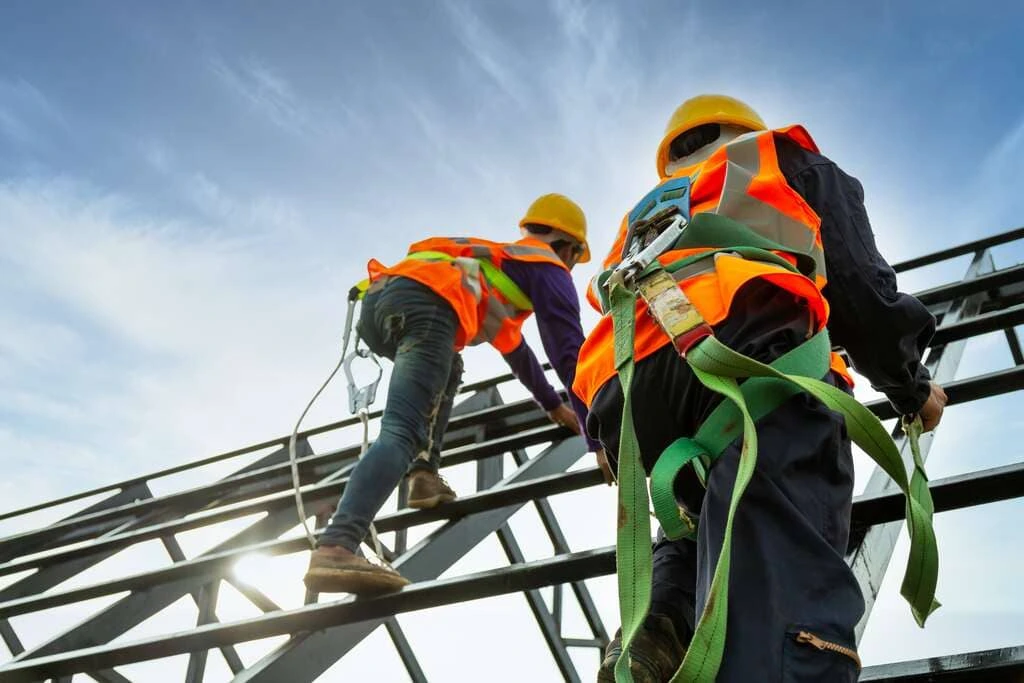 Workers wearing safety harnesses climbing a steel structure during height safety training.
