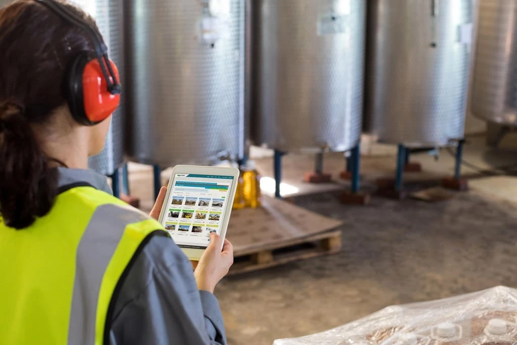An industrial employee with protective gear checks information on a digital tablet in a storage facility.