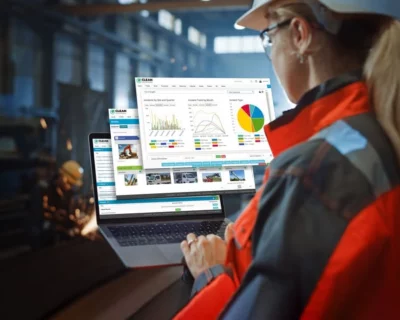 Industrial worker using a laptop with safety and productivity dashboards displayed inside a factory.