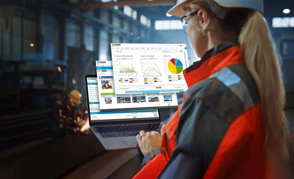 Industrial worker using a laptop with safety and productivity dashboards displayed inside a factory.