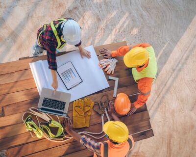 Workers in safety gear discussing digital toolbox talk materials on a construction site.