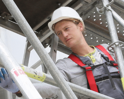 Construction worker with safety vest and hard hat on scaffolding at a U.S. job site.