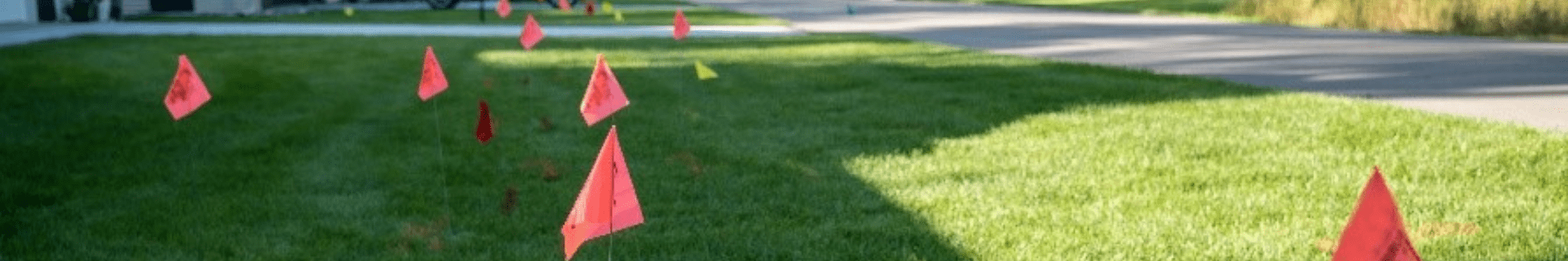 Red and yellow utility locate flags marking underground cables and pipelines in a suburban U.S. neighbourhood.