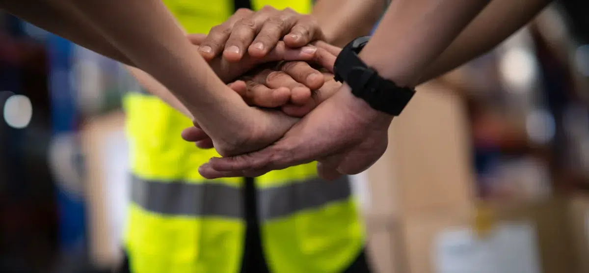Team of workers stacking hands to show unity and collaboration in workplace safety.