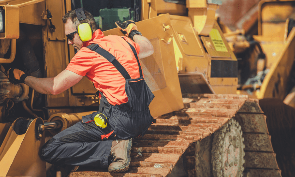 A man inspecting equipment on a job site. He's looking inside a excavators hood.
