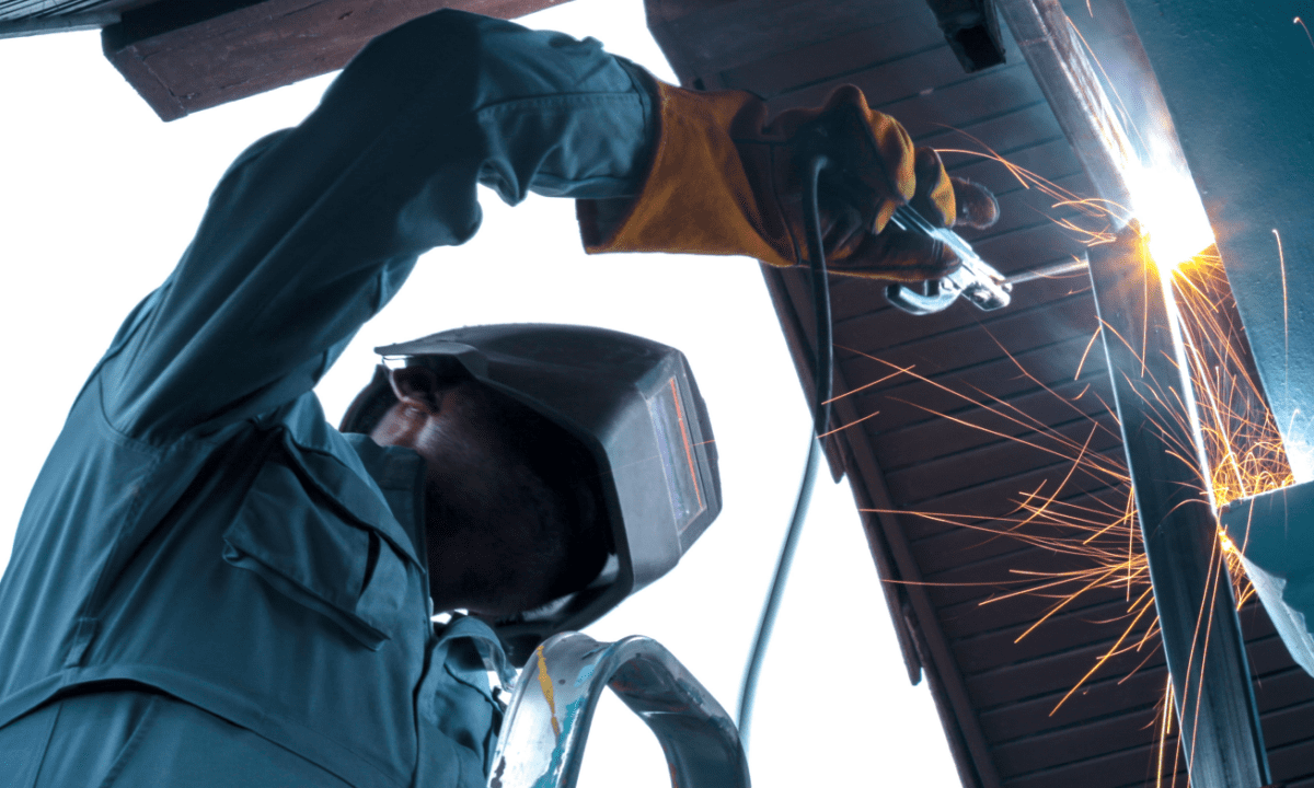 A welder works safely at his workplace while sparks and other debris protrudes from his torch.